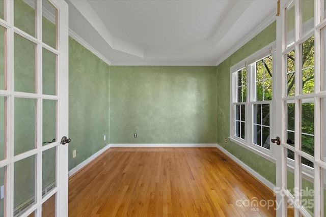 empty room with crown molding, a raised ceiling, baseboards, light wood-type flooring, and french doors