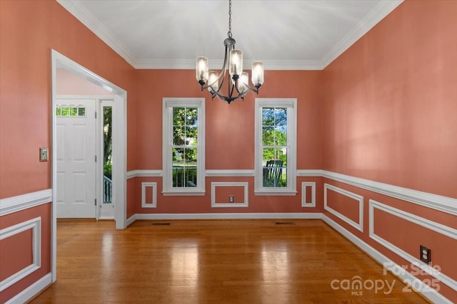 unfurnished dining area featuring wood finished floors, a chandelier, crown molding, and visible vents