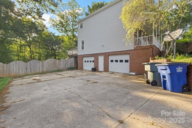 view of home's exterior featuring a garage, brick siding, fence, and driveway