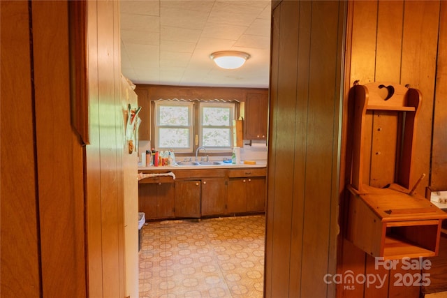 kitchen with a sink, wood walls, brown cabinetry, and light countertops