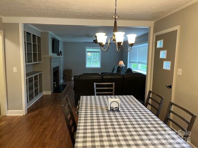 323 Hibriten Dr SE, Lenoir, NC 28645 - dining room with crown molding, a fireplace, baseboards, dark wood-type flooring, and a notable chandelier