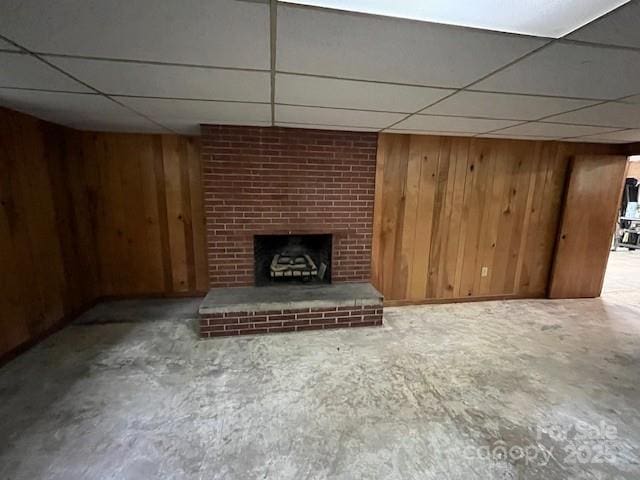 323 Hibriten Dr SE, Lenoir, NC 28645 - unfurnished living room with wooden walls, a brick fireplace, unfinished concrete floors, and a paneled ceiling
