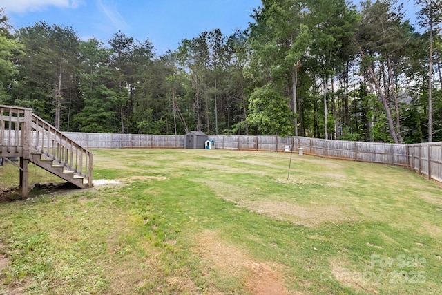 view of yard with a storage unit, a fenced backyard, stairway, and an outdoor structure