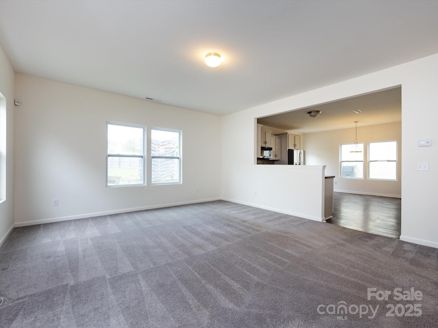 unfurnished living room featuring dark carpet and baseboards