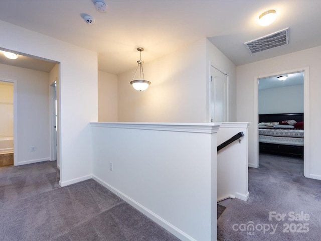 hall with an upstairs landing, carpet, visible vents, and baseboards