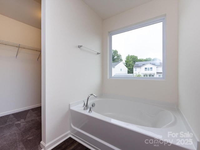 full bath featuring a garden tub, a walk in closet, and baseboards