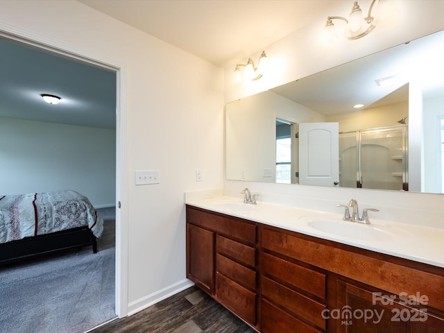 ensuite bathroom with double vanity, wood finished floors, an enclosed shower, and a sink