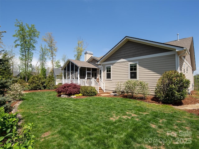 rear view of property with a lawn, a chimney, and a sunroom