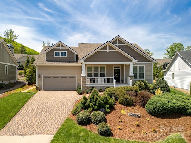 craftsman-style home featuring a porch, decorative driveway, and a shingled roof