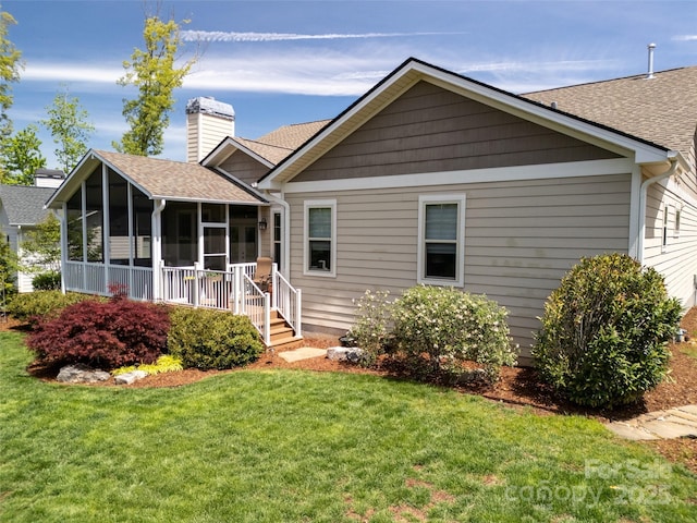 rear view of property with a sunroom, roof with shingles, a yard, and a chimney