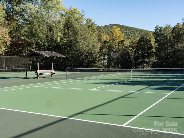 view of tennis court with a forest view and fence