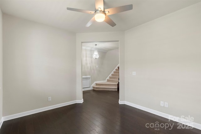 empty room with a ceiling fan, baseboards, dark wood-style floors, and stairs