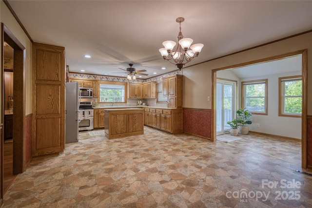 kitchen featuring appliances with stainless steel finishes, light countertops, stone finish floor, ceiling fan with notable chandelier, and a center island