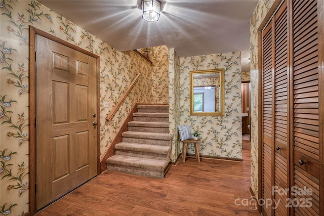 entryway featuring baseboards, wallpapered walls, wood finished floors, and stairway