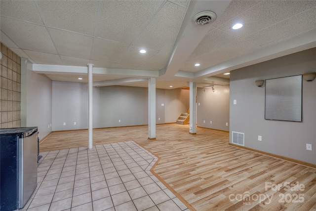 finished basement featuring visible vents, stairs, light wood finished floors, and baseboards