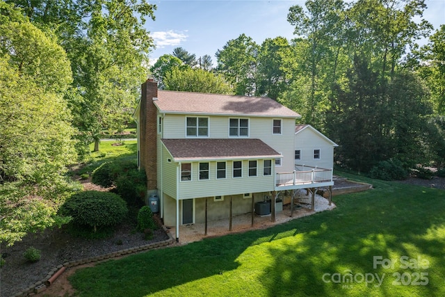 back of property featuring a shingled roof, a deck, central AC unit, a chimney, and a lawn