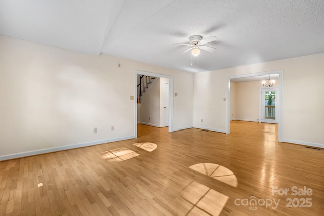 spare room with baseboards, light wood-style flooring, stairway, and ceiling fan with notable chandelier