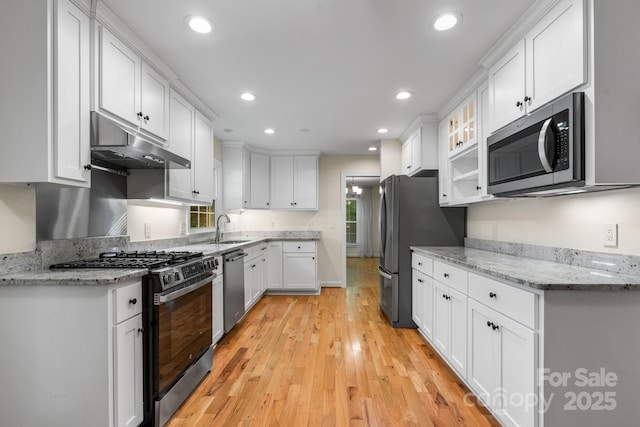 kitchen featuring light wood-style floors, white cabinetry, under cabinet range hood, a sink, and stainless steel appliances