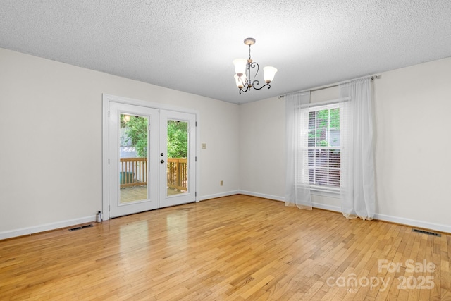 spare room with a textured ceiling, an inviting chandelier, light wood-style flooring, and visible vents