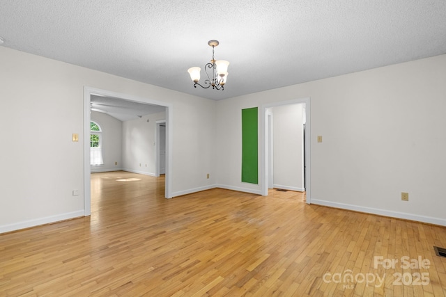 spare room featuring an inviting chandelier, baseboards, light wood-type flooring, and visible vents