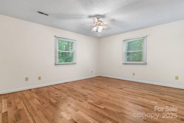 spare room featuring a textured ceiling, a ceiling fan, baseboards, light wood-type flooring, and visible vents