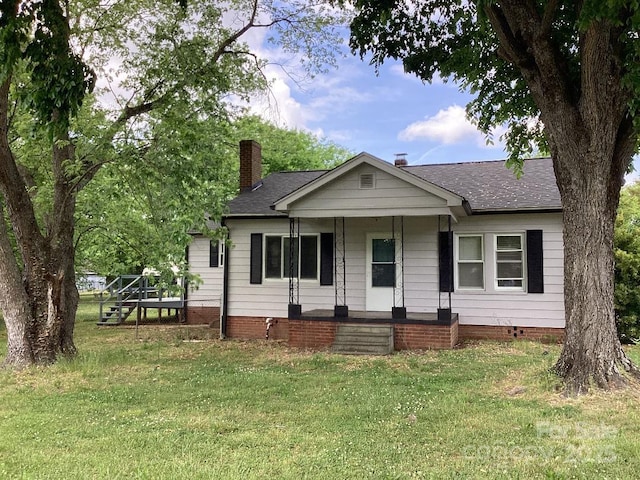 view of front of home featuring a chimney, a shingled roof, covered porch, and a front yard