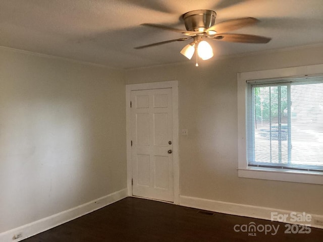 spare room with crown molding, a ceiling fan, baseboards, and dark wood finished floors