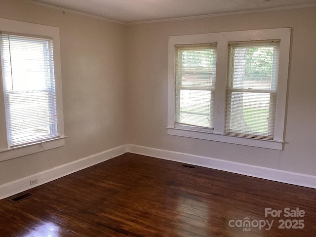 unfurnished room featuring crown molding, dark wood-style flooring, baseboards, and visible vents