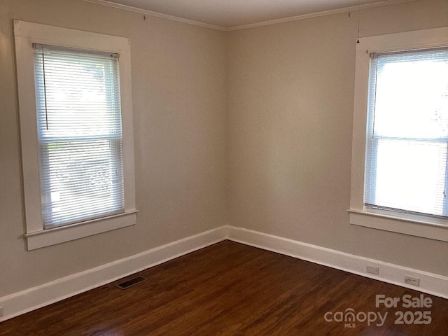 empty room featuring baseboards, ornamental molding, a wealth of natural light, and dark wood-type flooring