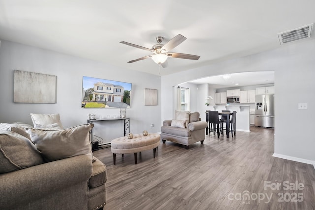 living room featuring arched walkways, wood finished floors, ceiling fan, baseboards, and visible vents