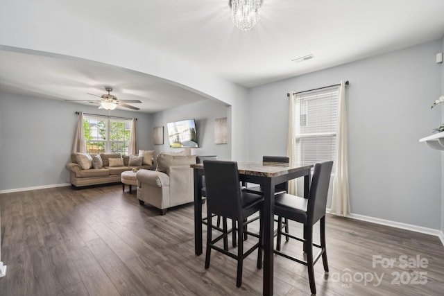 dining space with dark wood-style floors, visible vents, ceiling fan with notable chandelier, and baseboards