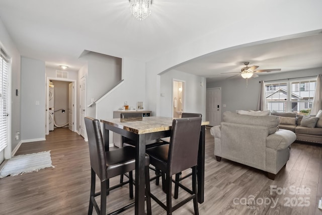 dining area featuring arched walkways, wood finished floors, stacked washer / drying machine, visible vents, and a ceiling fan