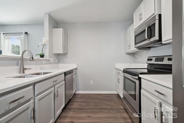 kitchen with light stone countertops, a sink, stainless steel appliances, baseboards, and dark wood finished floors