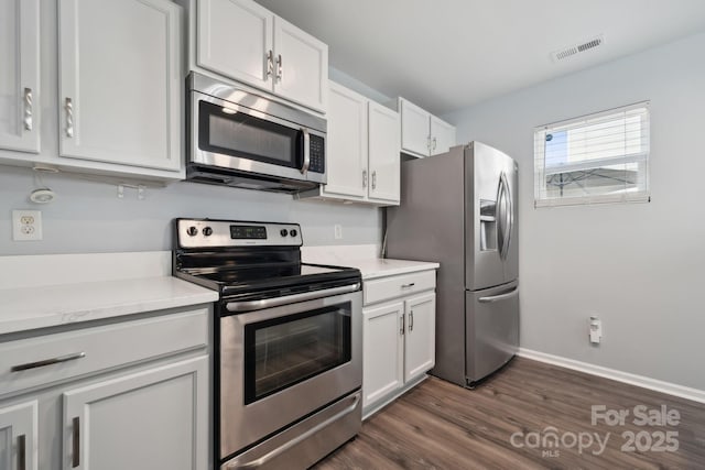 kitchen with dark wood-style flooring, stainless steel appliances, light countertops, visible vents, and baseboards