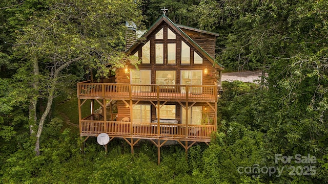 back of property featuring a view of trees, a wooden deck, and a chimney
