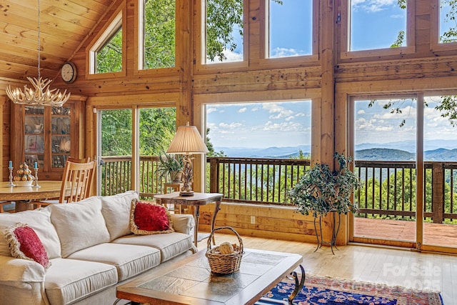 sunroom / solarium with an inviting chandelier, hardwood / wood-style floors, wooden walls, high vaulted ceiling, and a mountain view
