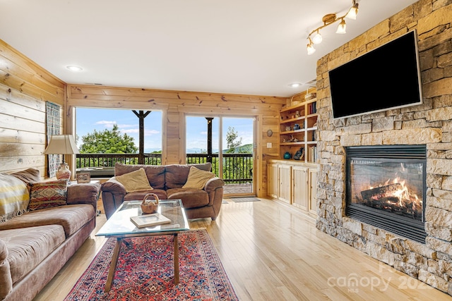 living area with a stone fireplace, recessed lighting, wooden walls, and hardwood / wood-style flooring