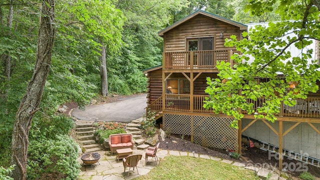 exterior space featuring stairs, log siding, an outdoor fire pit, and a patio area