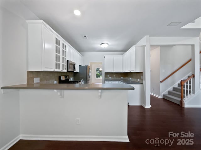 kitchen featuring a kitchen breakfast bar, tasteful backsplash, a peninsula, glass insert cabinets, and stainless steel appliances