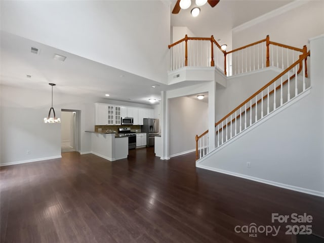 unfurnished living room featuring a towering ceiling, stairway, baseboards, ceiling fan with notable chandelier, and dark wood-type flooring