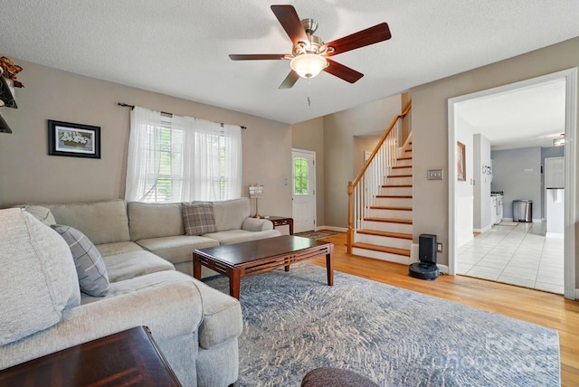 living room with a textured ceiling, stairs, a ceiling fan, baseboards, and wood finished floors