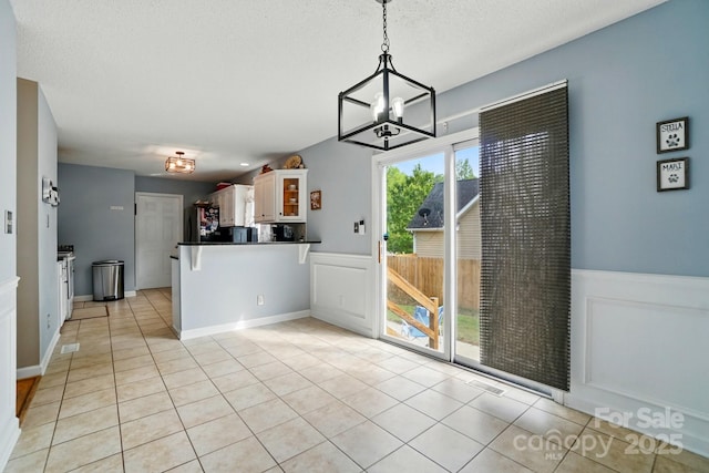 unfurnished dining area featuring an inviting chandelier, light tile patterned floors, and wainscoting