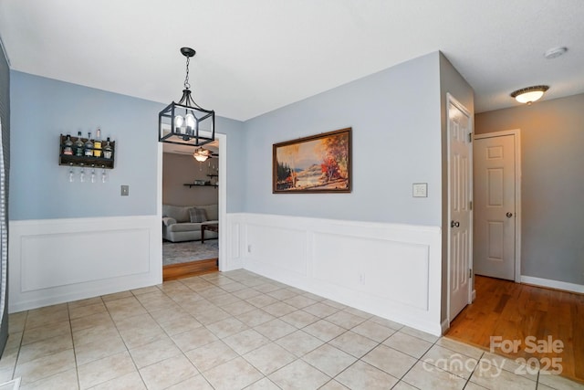 dining area featuring light tile patterned floors, a wainscoted wall, and a notable chandelier