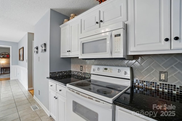 kitchen with white appliances, white cabinets, visible vents, and dark countertops