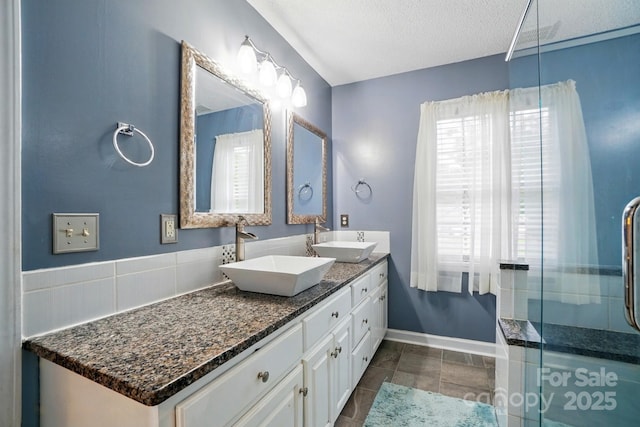 full bathroom featuring double vanity, a textured ceiling, a shower stall, and a sink
