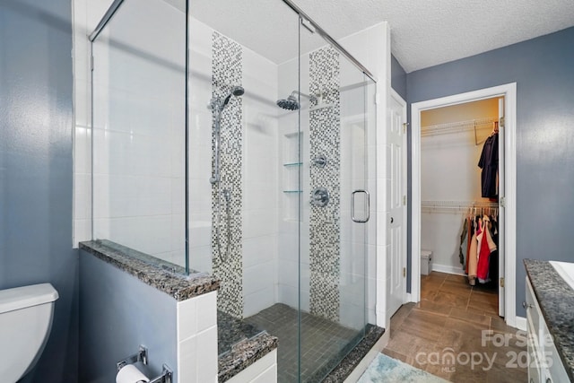 bathroom featuring toilet, a textured ceiling, a walk in closet, and a stall shower
