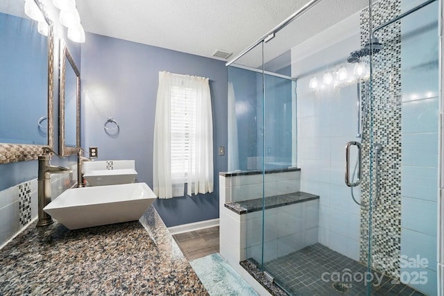 full bath with baseboards, a sink, a textured ceiling, and a stall shower