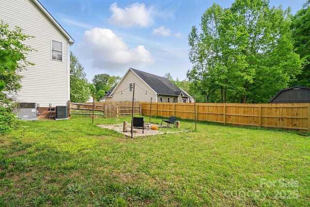 view of yard featuring central AC unit, a fenced backyard, and an outdoor fire pit