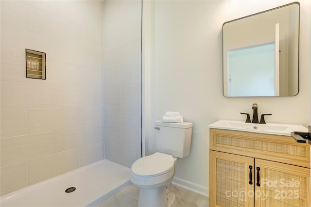 bathroom featuring vanity, baseboards, a tile shower, and toilet