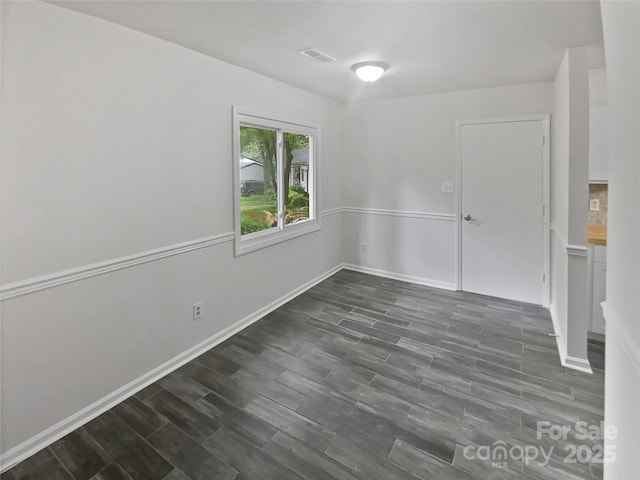 spare room with baseboards, dark wood-type flooring, and visible vents